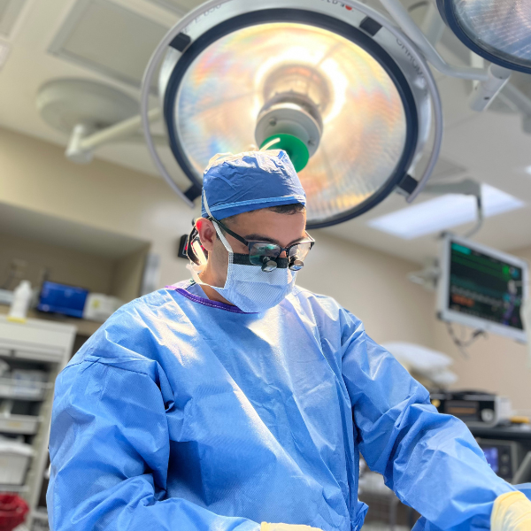 Dr Vaishnav performing a reconstructive procedure in a blue surgical coat and mask under lights